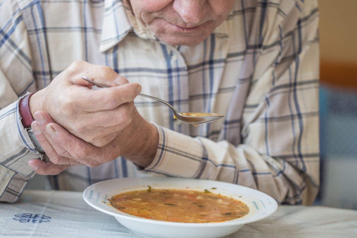 Pria makan sup dan menahan tangannya dari tremor akibat penyakit Parkinson