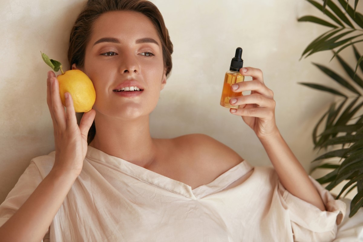 Seorang wanita dengan lemon dan sebotol ekstrak vitamin C di tangannya, vitamin yang membantu kulit