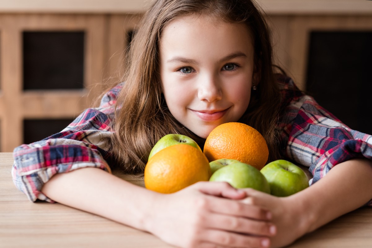 Vitamin C, dalam buah-buahan, seorang anak yang memegang jeruk dan apel di tangannya