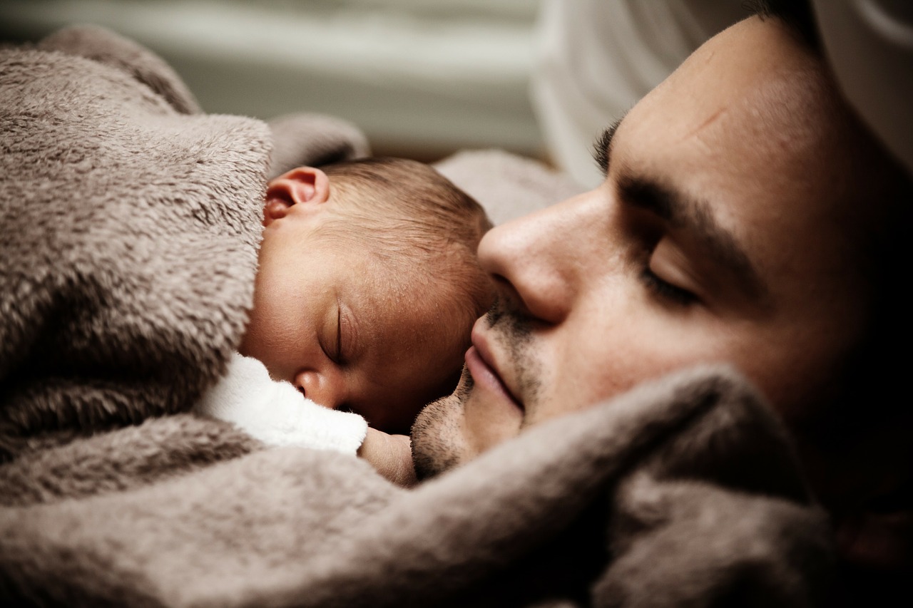 bayi tidur di samping ayahnya di bawah selimut cokelat