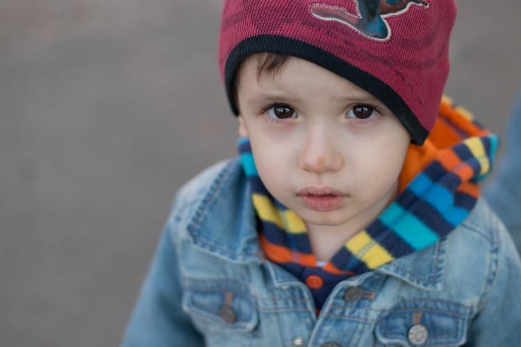 seorang anak dengan jaket biru dan topi merah yang melihat ke dalam lensa