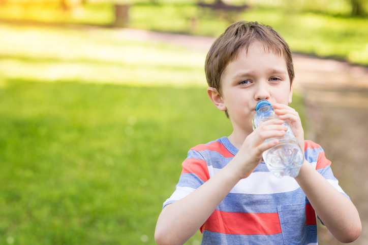 Anak laki-laki meminum air dari botol, dengan latar belakang rumput hijau