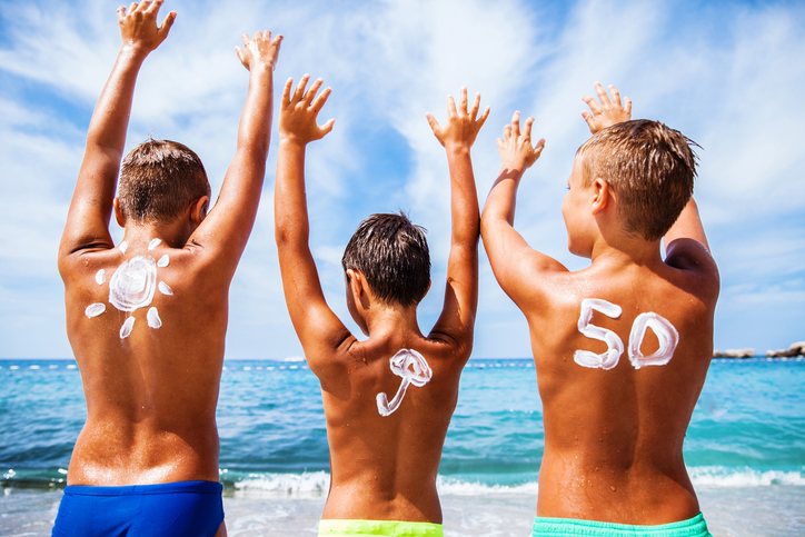 Tabir surya untuk anak-anak dengan OF 50, anak-anak berada di pantai di tepi laut dan bersenang-senang, tangan mereka terangkat