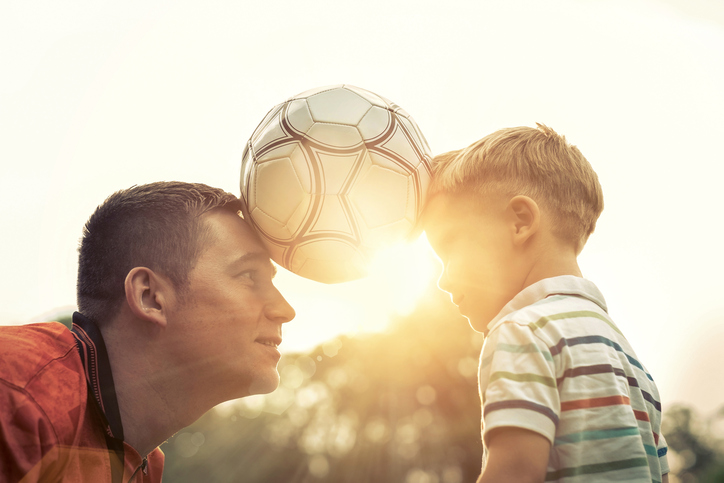 Ayah dan anak memegang bola di antara mereka.