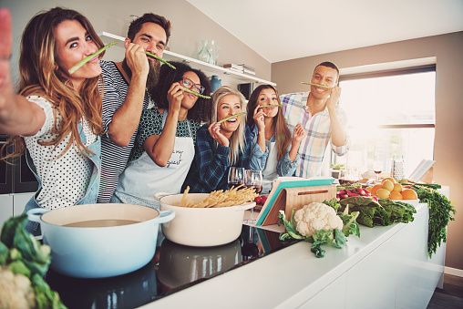 Orang-orang tersenyum saat mereka menyiapkan makanan. Mereka berada di belakang kompor.