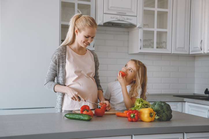 Ibu hamil dan anak perempuannya menyiapkan makanan sehat di dapur.