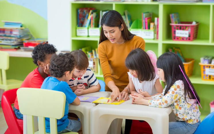 Seorang guru taman kanak-kanak membacakan sebuah buku untuk anak-anak