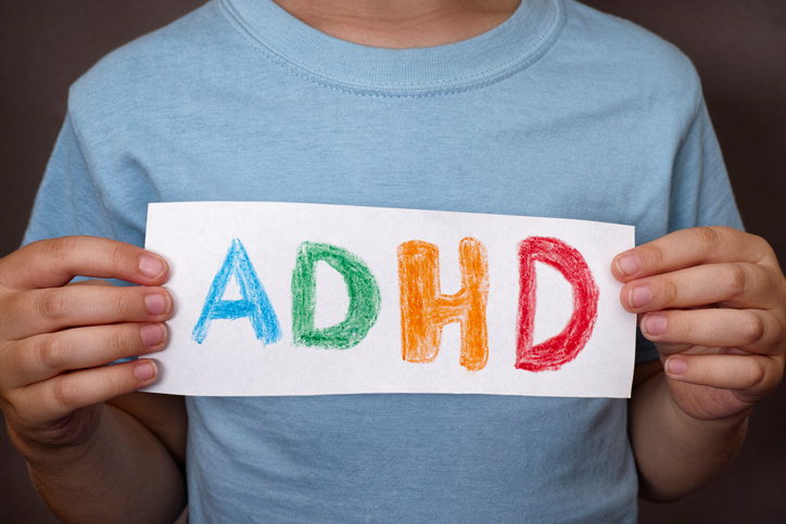 Seorang anak laki-laki memegang papan dengan tanda ADHD yang berwarna-warni