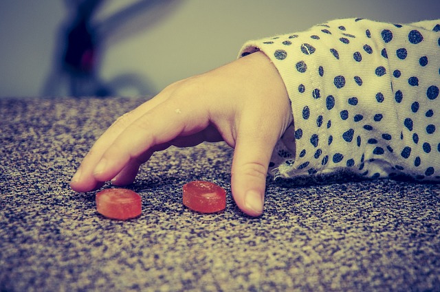 Tangan seorang anak, dua permen merah, kebiasaan makan yang buruk