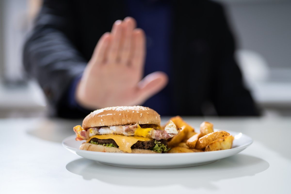 Makanan yang tidak pantas sebagai penyebab mulas - hamburger di atas piring yang ditolak seorang pria