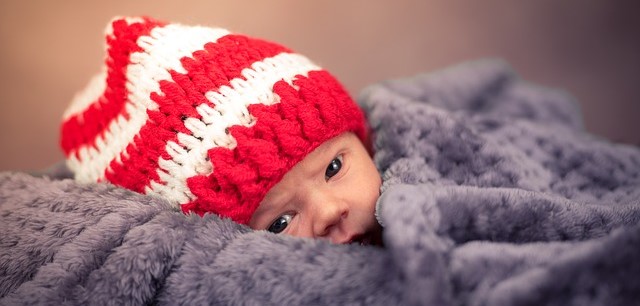 Seorang anak, berbaring berselimut, dengan topi bergaris merah dan putih